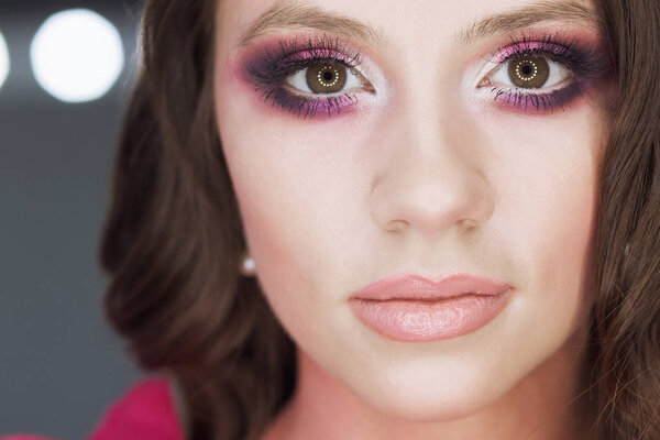 Crop view of attractive female with wavy hair pink lipstick and eye shadows posing at camera on blur background