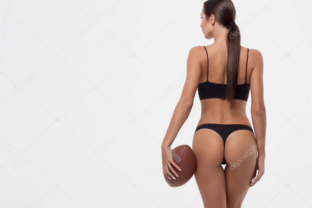 Back view of erotic young woman buttocks in lingerie holding rugby ball