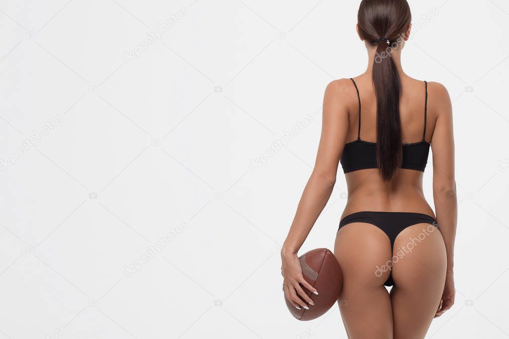 Back view of erotic young woman buttocks in lingerie holding rugby ball