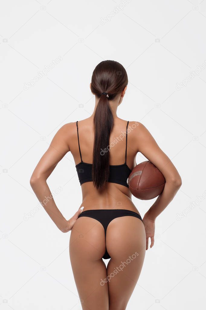 Back view of erotic young woman buttocks in lingerie holding rugby ball