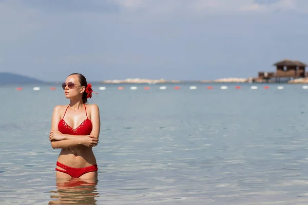 Beautiful woman walking in sea waterLovely young lady in red knitted swimwear looking away and walking in sea water while relaxing in wonderful resort