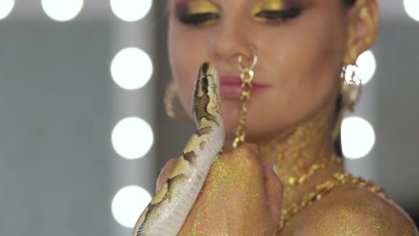 特写镜头中的女性 面容金黄 黑相间 手持蛇 在朦胧的背景下 用灯光凝视着摄像机 — 图库视频影像