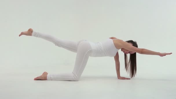 Фитнес-атлет женщина одета в белую спортивную одежду выполняет упражнения мост поднимая его одну ногу вверх — стоковое видео