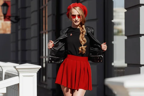 Portret van mooie jonge blonde vrouw het dragen van stijlvolle zwarte outfit, glimlachend op stedelijke achtergrond — Stockfoto