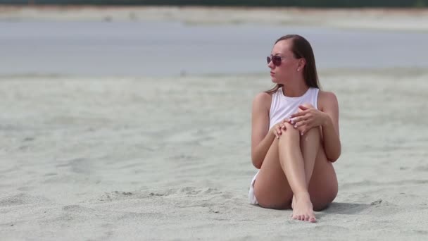 Languid woman sitting cross-legged on sand touching skin — Stock Video