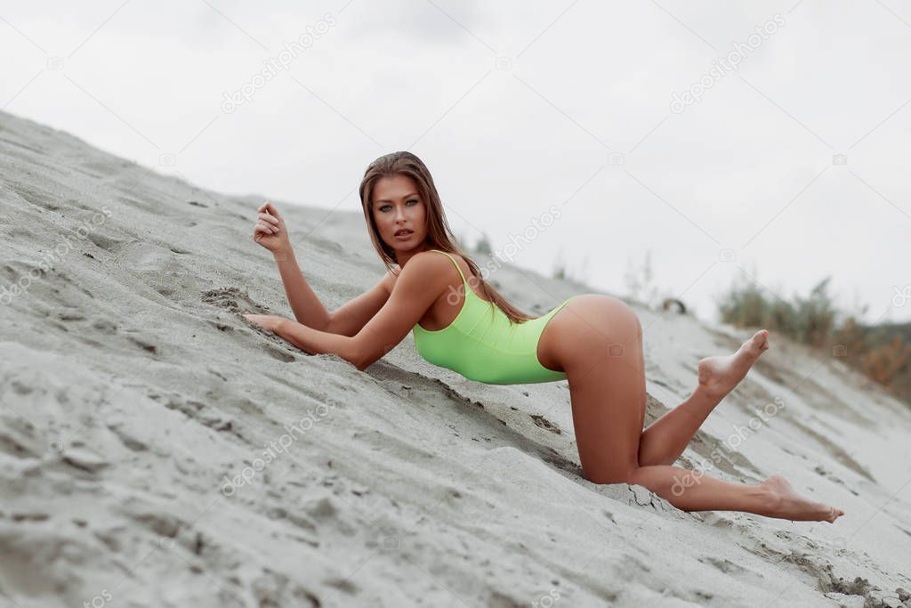 Seductive woman in stylish swimsuit kneeling in sand