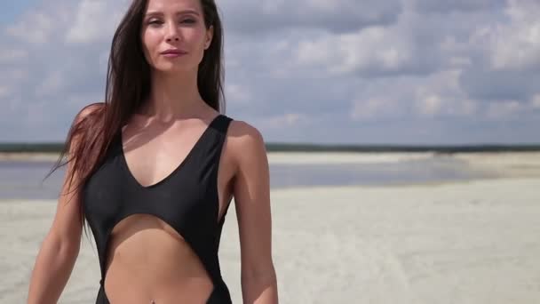 Hermosa mujer en traje de baño negro caminando a lo largo de la playa — Vídeos de Stock