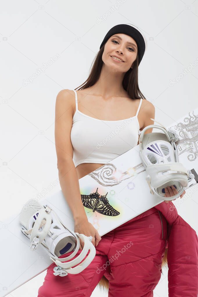 Active woman in open ski suit with snowboard in hands looking at camera