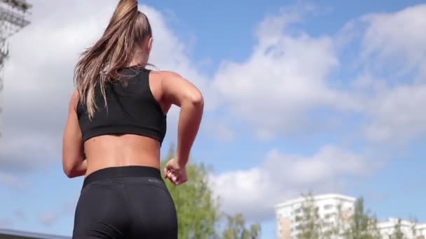 Mujer delgada corriendo en pista de carreras bajo el sol — Vídeo de stock