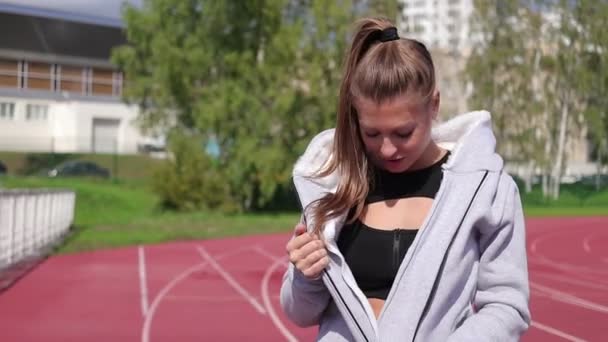 Schlanke athletische Frau setzt Kopfhörer auf, während sie auf dem Sportplatz steht — Stockvideo