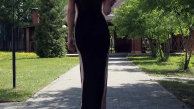 Bir kadeh şarapla köşkün bahçesinde yürüyen zarif bir kadın.