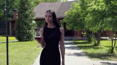 Bir kadeh şarapla köşkün bahçesinde yürüyen zarif bir kadın.