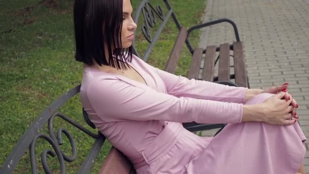 Elegancka młoda brunetka relaksująca się na ławce w parku — Wideo stockowe