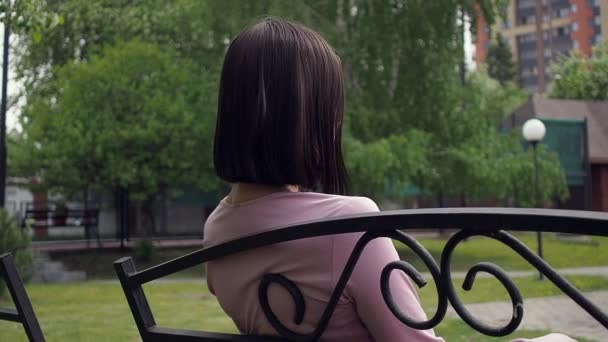 Elegante jonge brunette ontspannen op bank in park — Stockvideo