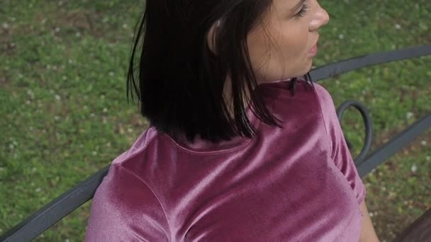 Елегантна молода брюнетка розслабляється на лавці в парку — стокове відео