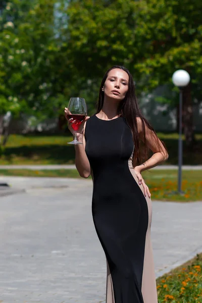魅力的な女性で黒エレガントなドレスは首に触れ 公園で晴れた夏の日に赤ワインを楽しむ — ストック写真