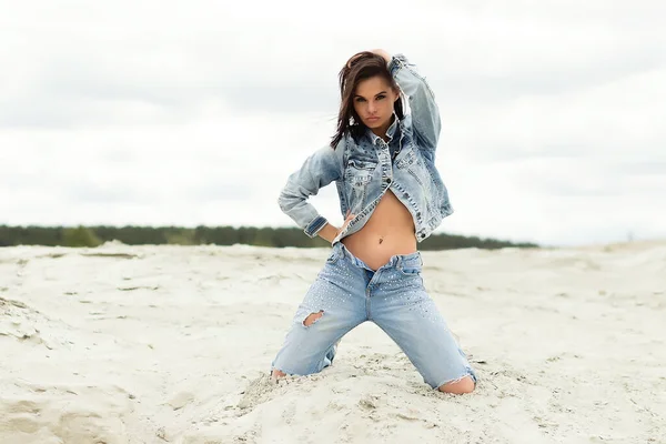 魅力的な女性モデルでジーンズでカメラを見て 田舎のぼやけた背景にデニムジャケットで胸をカバー — ストック写真