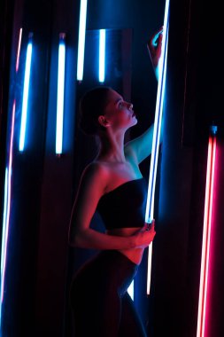 Parlak lamba ile tüm vücudu şehvetli kadın karanlık odada duvara yaslanmış neon ışıklı.