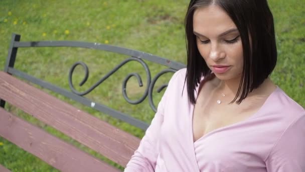 Elegante jonge brunette ontspannen op bank in park — Stockvideo