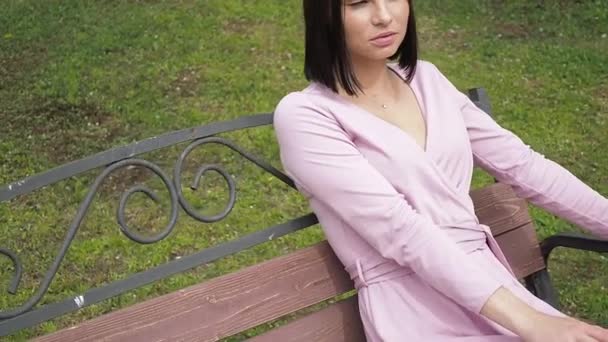 Elegantní mladá brunetka relaxační na lavičce v parku — Stock video