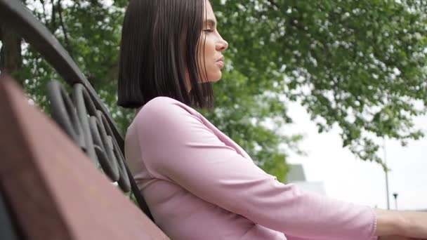 Elegante jovem morena relaxante no banco no parque — Vídeo de Stock