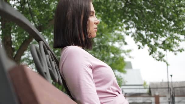 Elegancka młoda brunetka relaksująca się na ławce w parku — Wideo stockowe