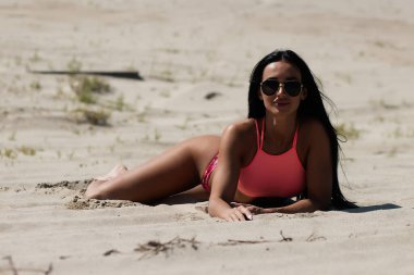 Pembe bluzlu, külotlu ve kumsalda yatıp güneşli yaz günlerinde plajda dinlenen modaya uygun kadın modeller.