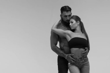 Siyah ve beyaz dövmeli üstsüz adam ve baştan çıkarıcı üstsüz kadın başka tarafa bakıyor.