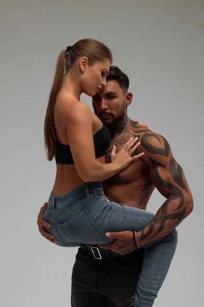 Muscular tattooed man embracing slim topless woman in panties on gray background