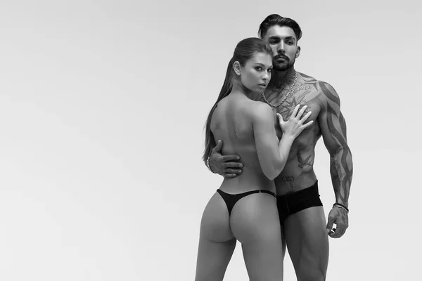 Black and white tattooed shirtless man and seductive topless woman looking away