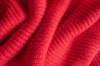 Texture of a knitted red sweater folded in a swirling pattern.