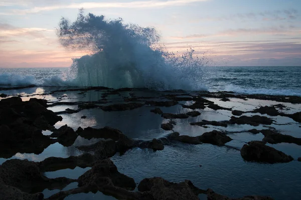 Splash van oceaan golven tegen een achtergrond van zonsondergang en rotsen — Stockfoto