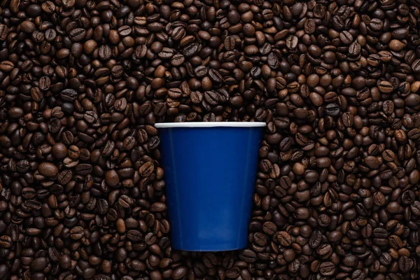 Blue disposable cup of coffee to go on the background of roasted beans.