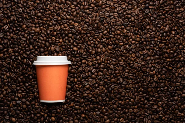 Orange disposable cup to go, on the background of coffee beans with empty space for text.