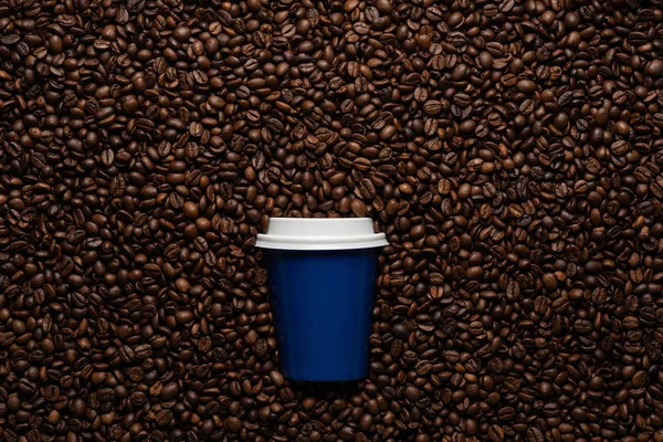 Blue disposable cup to go, on the background of coffee beans with empty space for text.