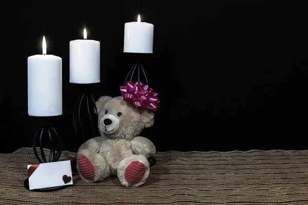 可爱的泰迪熊与粉红色的弓头 白色蜡烛栖息在黑色蜡烛持有人在网状的地方垫和木桌与卡和黑暗的背景 情人节 母亲节 复活节 圣诞节 婚礼概念 — 图库照片