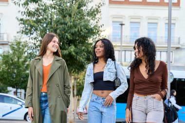 Üç farklı genç kadın şehir caddesinde keyifli bir gezinti yapıyor, canlı sohbetler yapıyor ve kahkahalarını paylaşıyorlar.