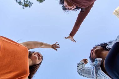 Üç neşeli genç kadın, birlik, takım çalışması ve ortak başarıyı simgeleyen bir kutlama jesti ile ellerini birleştiriyor.