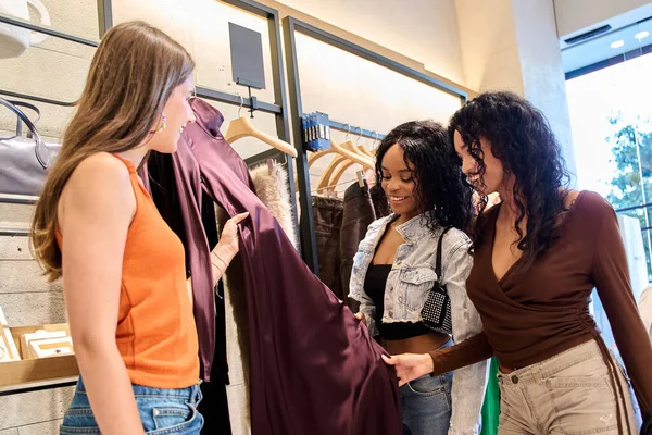 Üç bayan arkadaş eğlenceli bir alışveriş gününün tadını çıkarıyorlar. Canlı bir giyim mağazasında şık bir elbiseyi inceliyorlar.