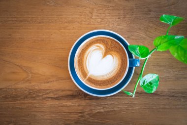 Güzel, mavi bir fincan sıcak kapuçino kahve, ahşap sehpanın üzerinde latte sanatı, içki arka planı için seçici odak.