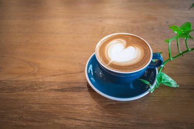 Güzel, mavi bir fincan sıcak kapuçino kahve, ahşap sehpanın üzerinde latte sanatı, içki arka planı için seçici odak.