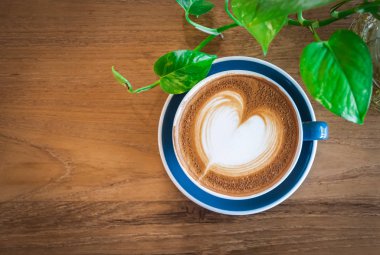 Güzel, mavi bir fincan sıcak kapuçino kahve, ahşap sehpanın üzerinde latte sanatı, içki arka planı için seçici odak.