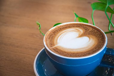 Güzel, mavi bir fincan sıcak kapuçino kahve, ahşap sehpanın üzerinde latte sanatı, içki arka planı için seçici odak.