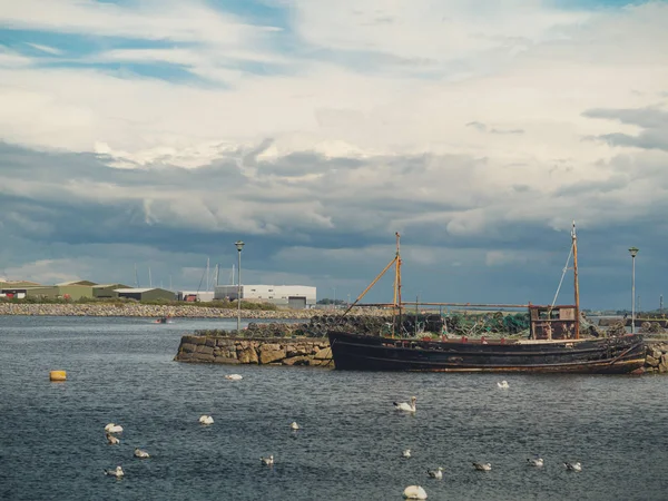 Vieux bateau de pêche et colonie de cygnes blancs, Claddagh, Galway, Irlande, ciel nuageux . — Photo