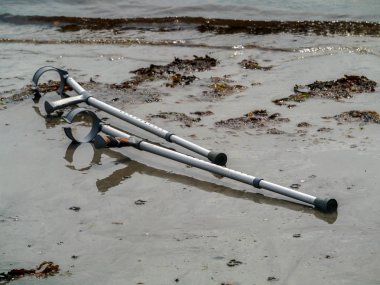 Su kenarındaki kumda eski kullanılmış koltuk değnekleri. Konsept sağlık, Su kurtarma prosedürü.