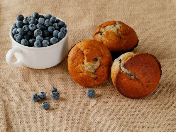 Drie blueberry muffins en beker met verse bessen op een Hessische oppervlakte. Stilleven. Landelijke stijl. — Stockfoto