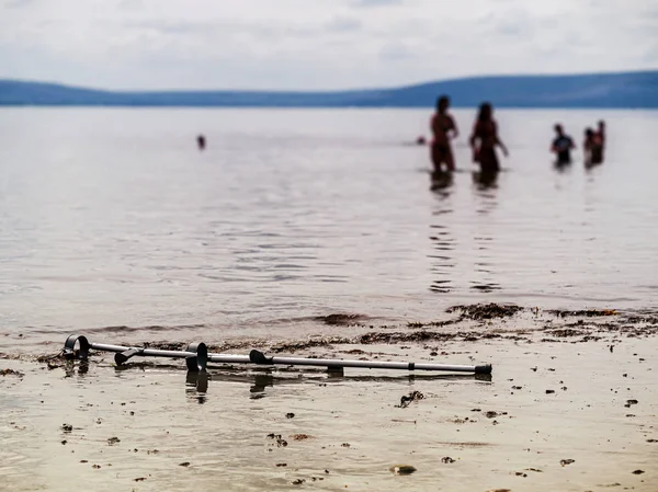 Crutches on a sand by water. People silhouettes in water, Selective focus. Concept healthcare, Water recovery procedure.