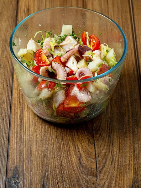 Ahşap bir masada cam bir kase taze ahtapot salatası, Portre oryantasyon, sağlıklı gıda.