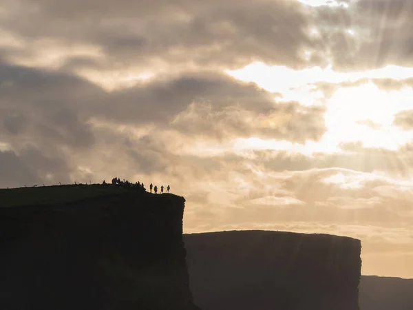 Cliff of Moher silhouet en toeristen, dramatische hemel, zon flare en stralen. County Clare, Ierland. — Stockfoto