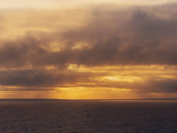 Sunset sky over ocean's surface, warm orange tones, waves.